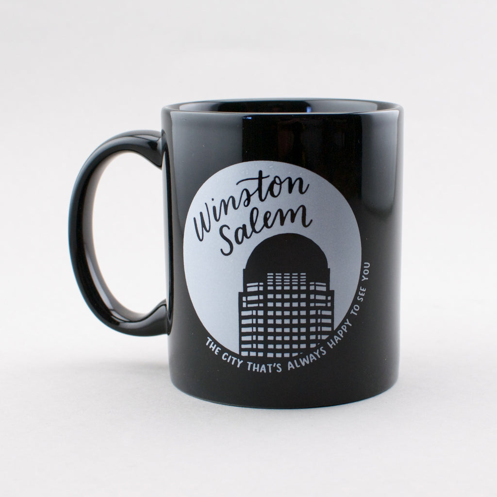Winston-Salem: the city that's always happy to see you. Black ceramic mug with white print, by Em Dash Paper Co.